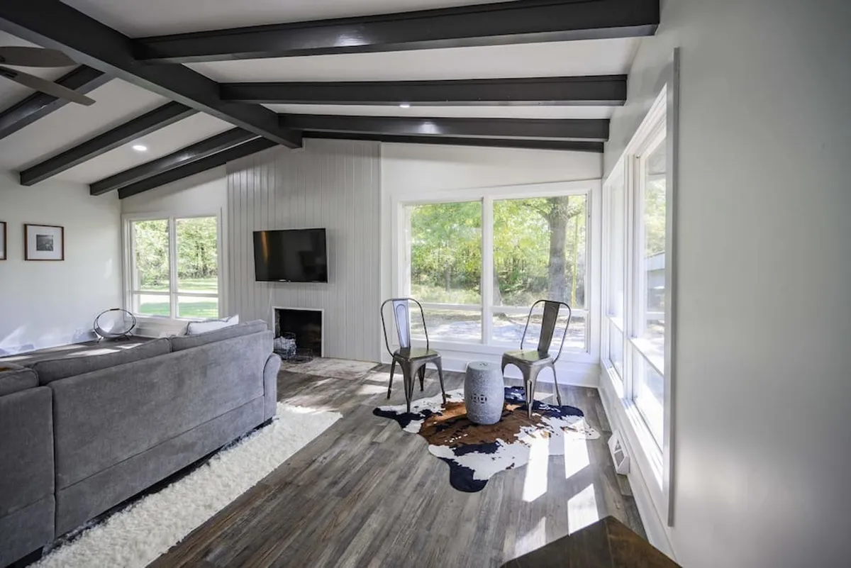 A comfortable living room with modern sofa, cowhide rug, and a wall-mounted TV, flooded with natural light from large windows. The seating invites relaxation and conversation, while the TV is ideal for shared entertainment.