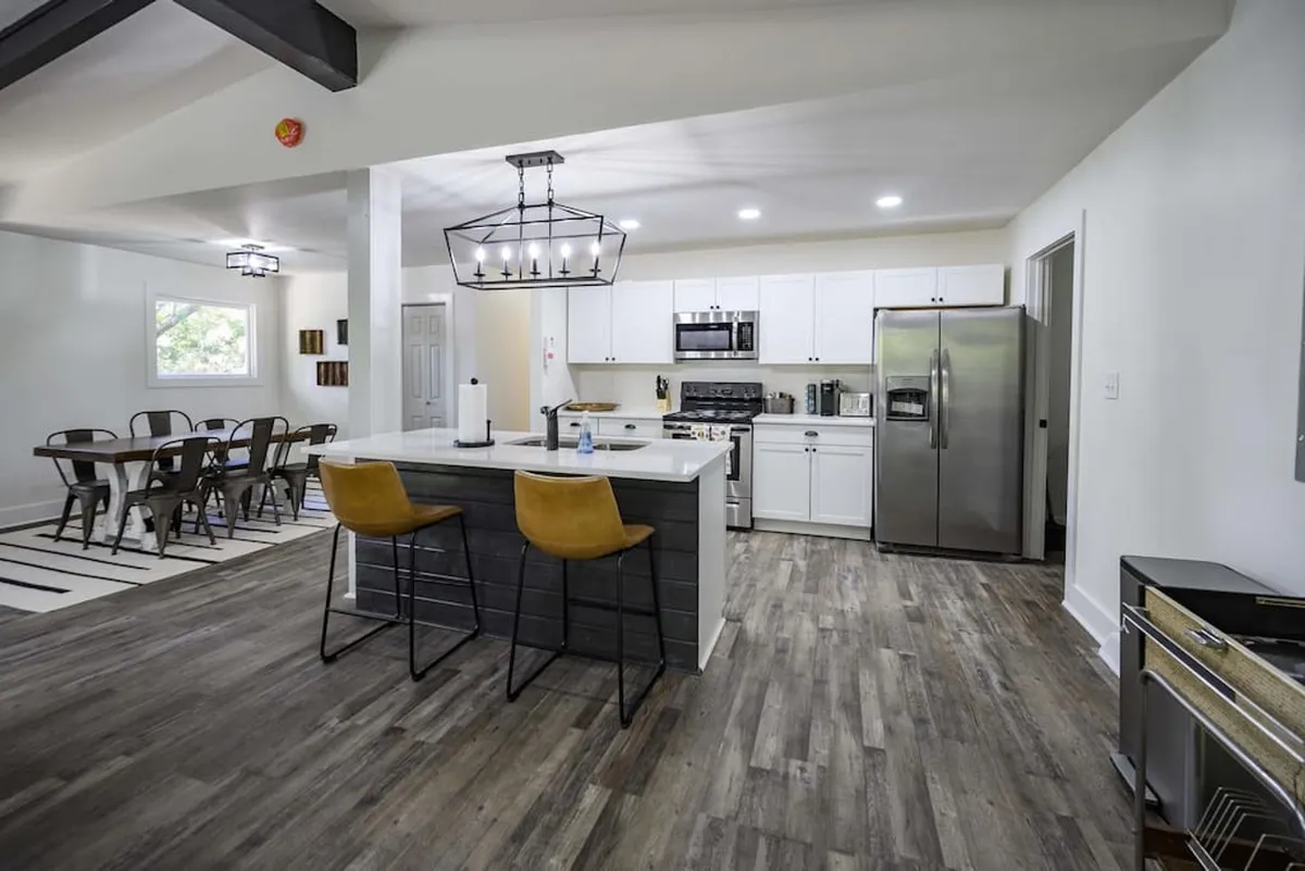 A view centered on the kitchen island with stools, adjacent to a welcoming dining table and modern appliances. The layout is ideal for shared meals, casual chats, or festive gatherings, with an inviting, communal ambiance.