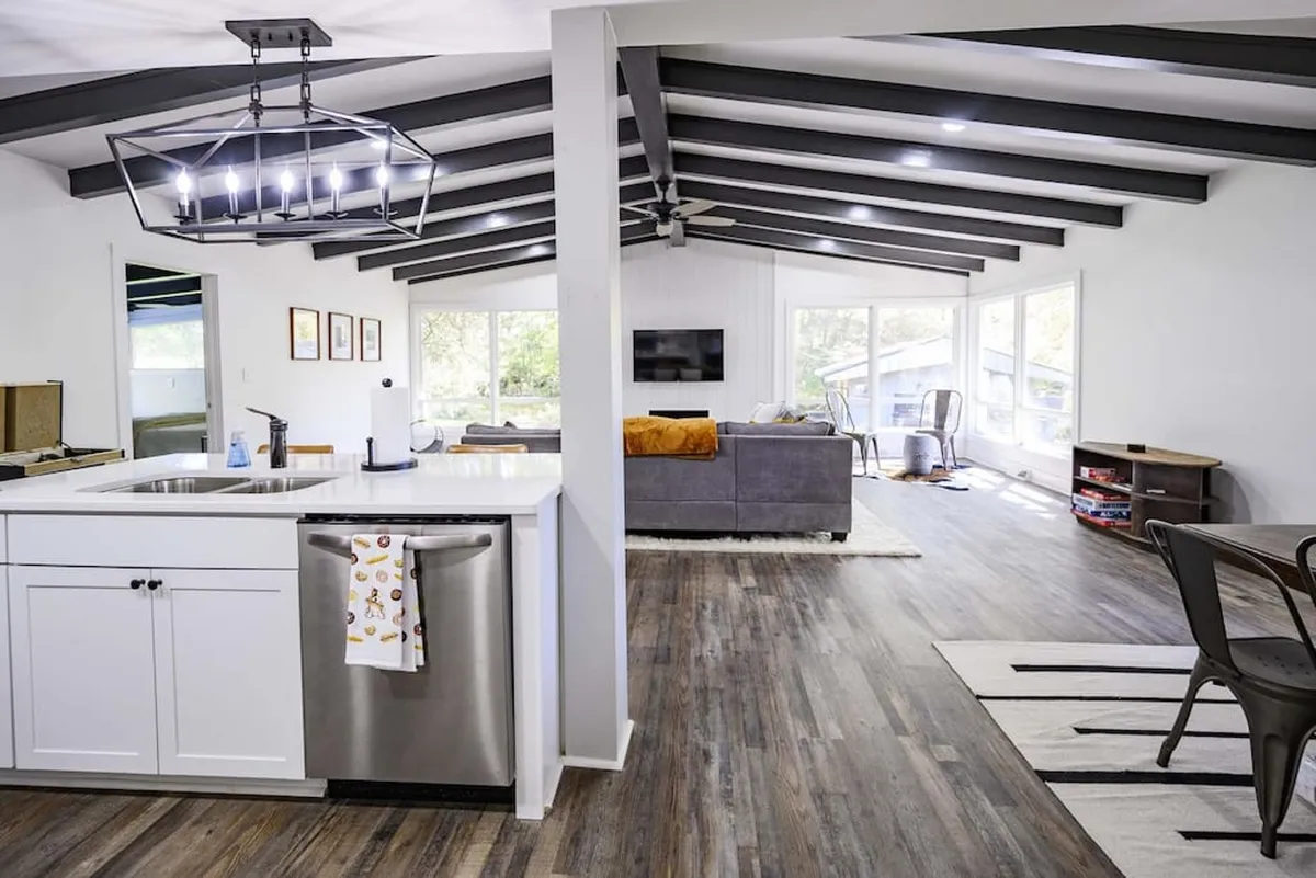 This image features an open-plan living area, blending a modern kitchen island, comfortable sofa, and spacious dining area. Large windows invite natural light, creating an inviting atmosphere ideal for gatherings.