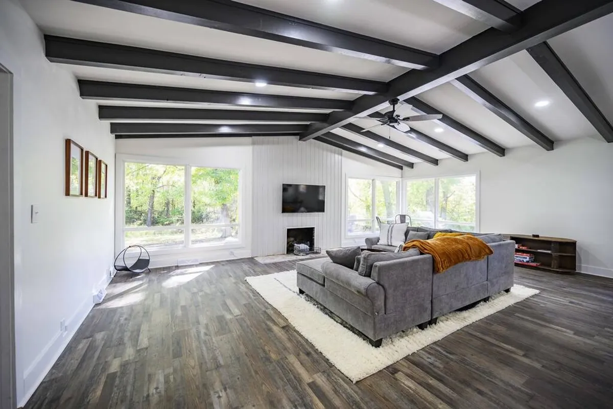 The photo highlights a cozy living room with a plush sofa, large windows, a fireplace, and a TV. The mood is warm and inviting, suggesting a space well-suited for unwinding after a busy day or connecting with loved ones.