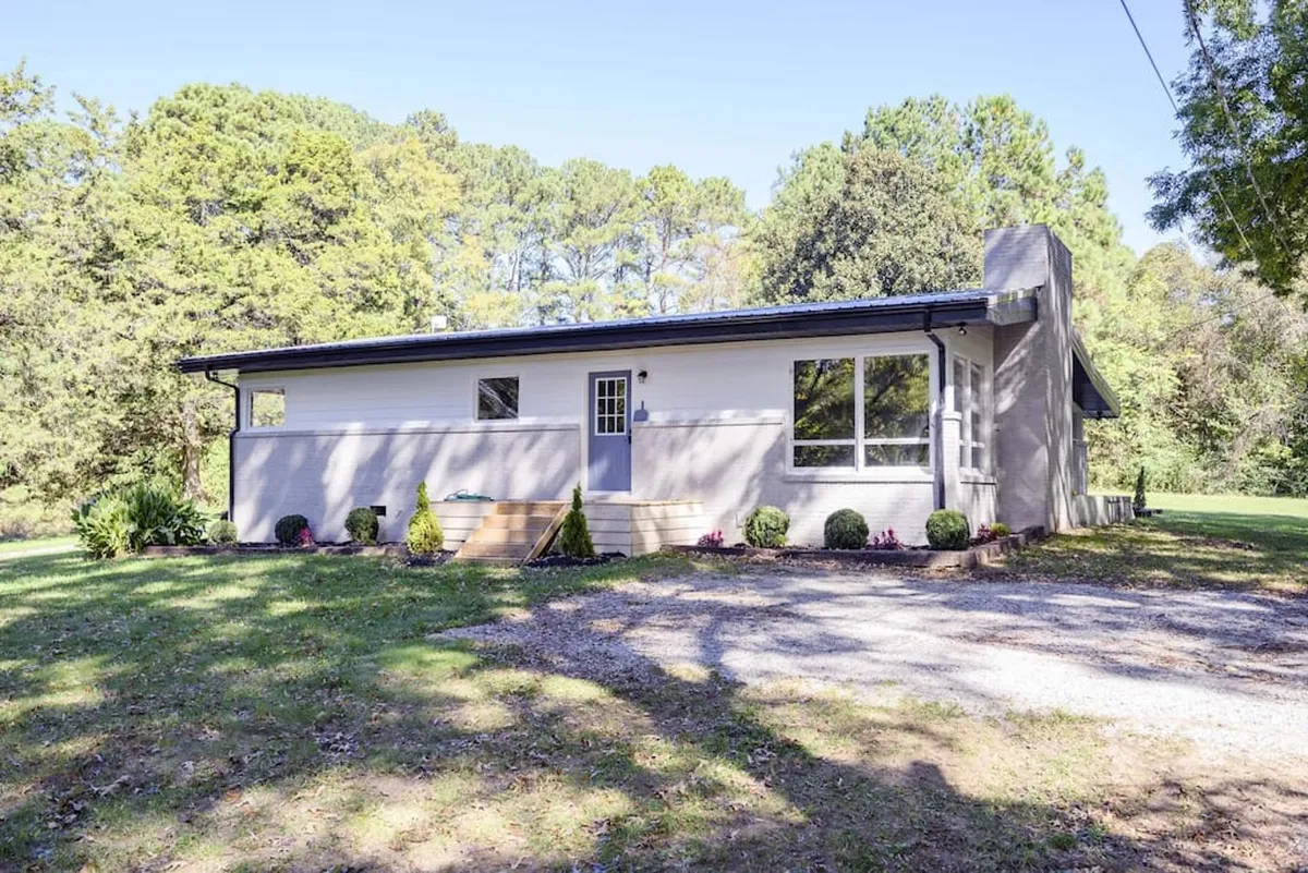 This exterior image showcases the modern facade of the home surrounded by a landscaped garden. Large windows invite natural light, and the welcoming porch offers a clear connection to the outdoors, hinting at the home's proximity to nature trails and lakes.