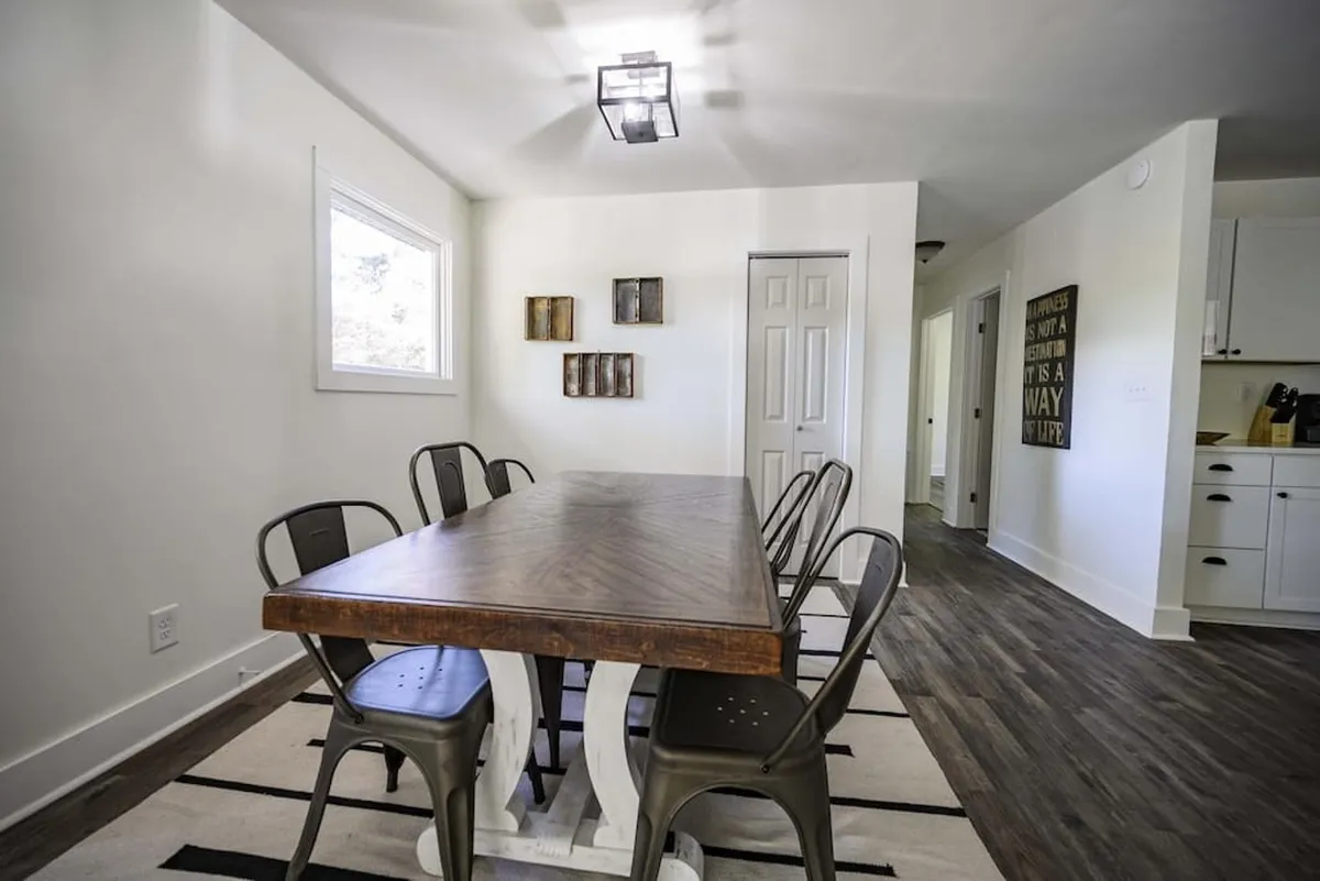 A large wooden dining table surrounded by metal chairs with decorative wall art sets a lively, communal scene. The space exudes warmth, making it ideal for festive group meals and celebrations.