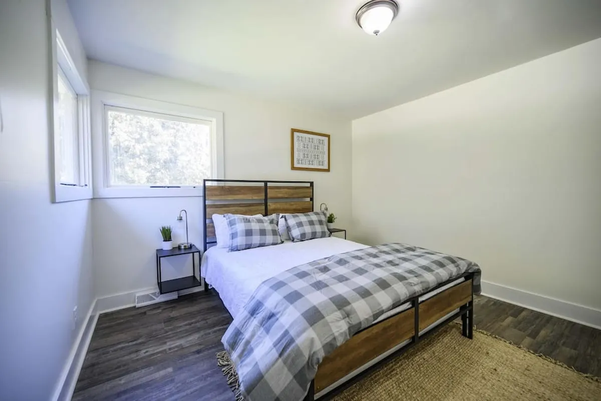 A cozy bedroom with plaid bedding, a nightstand lamp, framed artwork, and a window that brings in gentle morning light. The room feels restful and inviting, with a clear focus on the comfort of a peaceful night's rest and the refreshing energy of a new day.