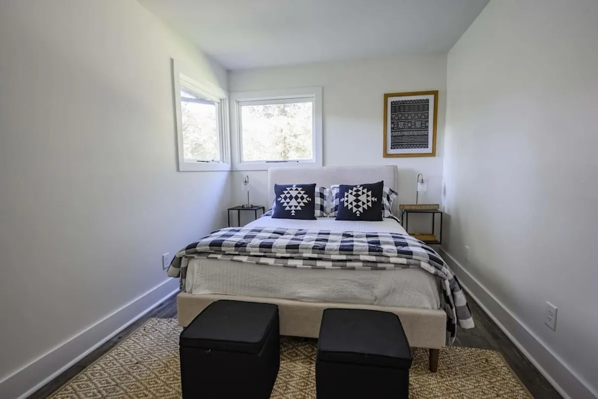 This image features a cozy bedroom with a bed adorned in patterned bedding, decorative wall art, and nightstands with soft-glowing lamps. Natural light pours into the space, creating an inviting and serene atmosphere perfect for unwinding.